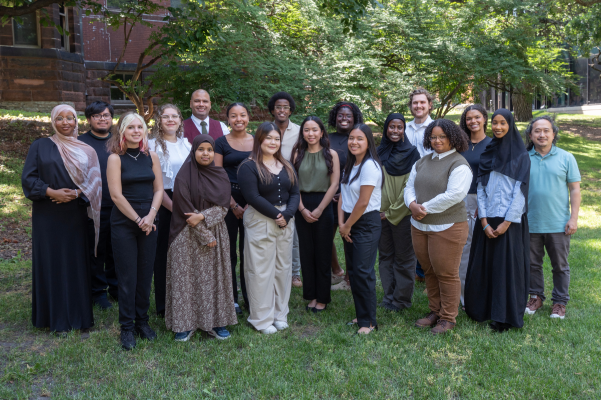 18 students standing on grass with trees and shrubs in the background